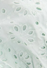 Tissu en coton vert menthe léger présentant une broderie florale complexe avec des détails découpés, mettant en valeur un design délicat et texturé.