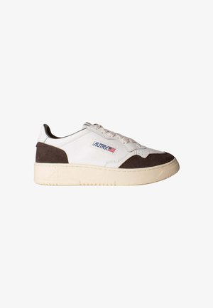 Zapatilla blanca de perfil bajo con detalles en ante marrón, suela crema, cordones y una etiqueta con el logo y la bandera americana en el lateral.
