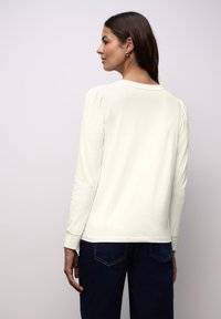 Top met lange mouwen in off-white, met een ronde halslijn en subtiele pofschouders. Gecombineerd met donker denim, minimalistisch ontwerp.