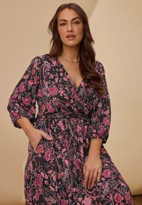 Black dress with a vibrant pink floral pattern, featuring long sleeves, a V-neck, and a cinched waist with a tie, includes side pockets.