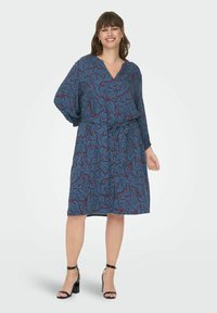 Robe à motifs floraux bleus avec un décolleté en V, des manches longues, une ceinture à nouer soi-même et une longueur mi-genoux. Présente des accents bordeaux audacieux.