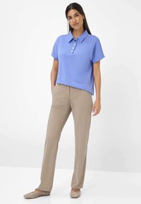 Polo shirt azzurro chiaro a maniche corte con tre bottoni, abbinato a pantaloni beige su misura. Il modello è in piedi con le mani nelle tasche, indossando scarpe chiare.