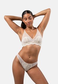 Sheer cream bralette ja vastaava thong-pohja, jossa on pitsireunukset; kukkakuvioiset pitsikoristeet ja säädettävät ohuet hihnat. Pehmeä, herkkä rakenne.
