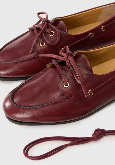 Burgundy leather shoes with a smooth texture, lace-up design, and gold eyelets. Includes a matching lace. Rounded toe and stitched detailing.