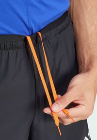 Blue athletic shirt with black shorts; orange drawstrings held in a hand. The material appears smooth with a flat texture.