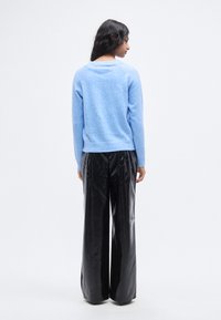 Απαλό γαλάζιο πλεκτό πουλόβερ με χαλαρή εφαρμογή και ριμπ τελείωμα, σε συνδυασμό με ψηλόμεσα μαύρα παντελόνια από συνθετικό δέρμα με φαρδιά μπατζάκια.