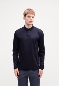 Dunkelblaues Langarm-PoloheMD mit einem geknöpften Kragen, das ein dezentes Logo auf der Brust und einen glatten, strukturierten Stoff aufweist.