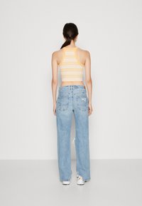 Top corto a rayas amarillas y blancas combinado con jeans de tiro alto, de corte holgado, en azul claro, que presentan detalles desgastados y dobladillos deshilachados.