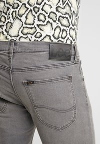 Jean en denim gris avec poche arrière et étiquette noire de la marque Lee, associé à un haut imprimé serpent rentré à l'intérieur.
