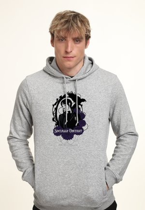 Man wearing light grey hoodie with black and purple graphic of a woman, raven, flowers, and the text "Socially Distant" on front.