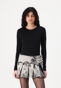 Un haut noir à manches longues assorti à une jupe en denim plissée grise arborant un motif tie-dye et plusieurs accents de boucles à la taille.
