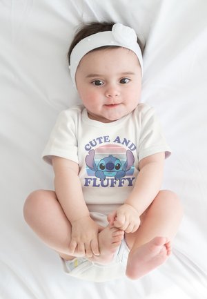 Witte katoenen jumpsuit met de tekst "CUTE AND FLUFFY" en een Stitch-illustratie. Kind met donker haar, draagt een witte haarband met een bloemenaccent.