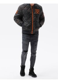 Sort quiltet bomberjakke med orange detaljer, lynlås og logopatch. Kombineret med slidte grå skinny jeans og sorte sneakers.