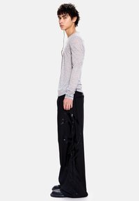 Pilkas ilgomis rankovėmis marškinėlis derinamas su juodomis plačiomis kelnėmis, puoštomis blizgiu abstrakčiu raštu. Modelis stovi šonu, dėvi juodus batus.