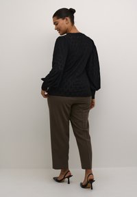 Top negru texturat cu mâneci lungi bufante, asortat cu pantaloni drepti maro și sandale cu vârful descoperit negre. Model subtil cu diamante pe top.