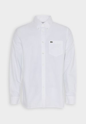 Chemise blanche à manches longues avec boutons en coton, dotée d'un col, d'une poche avant et d'un petit logo vert sur la poche poitrine.
