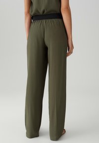 Olijfgroene, wijde broek met een zwarte elastische tailleband, gemaakt van lichtgewicht stof, met een gladde textuur en een ontspannen pasvorm.