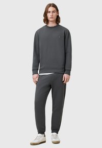 Sudadera gris y pantalones de chándal a juego, hechos de una tela suave. La sudadera tiene un cuello redondo y un logo minimalista; los pantalones tienen puños elásticos.