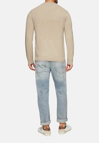 Bežs adīts džemperis ar garām piedurknēm, apaļu kakla izgriezumu un ribotām aprocēm, kopā ar gaiši zilām nolocītām džinsām un baltām kedām.