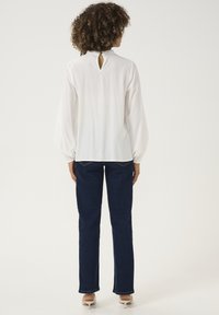 Blusa bianca a maniche lunghe con un design a chiave nella parte posteriore, abbinata a jeans in denim blu. La blusa presenta maniche larghe e una trama morbida.