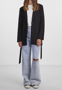 Černý dlouhý blejzr s jednobottonovým zapínáním, kombinovaný se světle modrými roztrhanými džíny a černými teniskami. Silueta je uvolněná a mírně oversized.