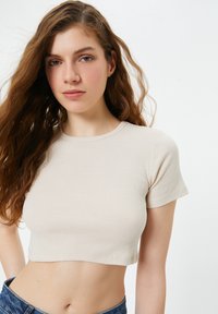 Beige geribbelde crop top met korte mouwen en een ronde halslijn. Heeft een aansluitend ontwerp dat de torso accentueert, in combinatie met denim.
