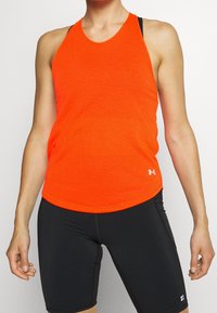 Ljusa orange ärmlösa atletiska topp med ett mönster, rund halsringning och en logotypaccent vid nederkanten, ihop med svarta shorts.