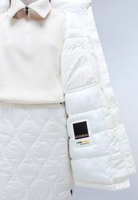 Hvid pufferjakke med quiltet mønster, halvlynlås, stående krave. Funktioner Cordura-label og elastisk detalje på ærmet. Blød tekstur.