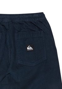 Shorts en velours côtelé bleu marine avec une ceinture élastique, dotés d'une poche arrière unique et d'une patch logo noir. Surface texturée avec des côtes verticales.