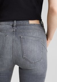 Grå denimjeans med en åtsittande design, som har två bakfickor och en läderlogotyp på midjan. Slät struktur.