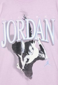 Világoskék lila póló, amelyen egy kosárlabdajátékos ugrás közben látható grafikával, és a "MICHAEL JORDAN" felirat vastag, színes betűkkel.