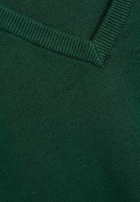 Dunkelgrüner Pulloverstoff mit einem gerippten V-Ausschnitt und einer glatten Textur, die gleichmäßige Nähte und ein weiches, gestricktes Muster betont.