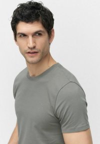 Grå bomulds T-shirt med runde halsudskæring og korte ærmer, der har en glat tekstur og en tætsiddende pasform, båret af en mand.