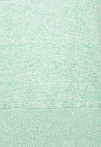 Ljust grönt strukturerat tyg med en melerat mönster, bestående av ett mjukt, stickat material med en jämn, subtil färgvariation.