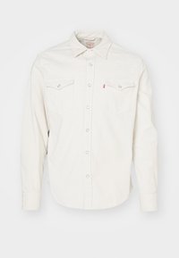 Chemise en jean blanche à manches longues avec fermeture à boutons, deux poches avant à rabat avec boutons, et col pointu.