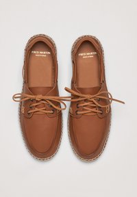 Zapatos de cuero marrón con punta redondeada, diseño de cordones y detalles cosidos alrededor de la suela. Nombre de la marca visible en la plantilla.