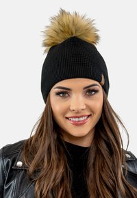 Zwarte gebreide beanie met een geribde rand en een grote nepbont pompon bovenop. Kleine merklabel zichtbaar aan de zijkant.