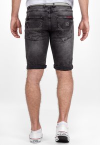 Donkergrijze denimshorts met omgeslagen zomen, voorzien van twee achterzakken met stiksels, en gedragen met witte sneakers.