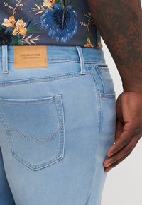 Svijetloplave traperice s kožnom oznakom "JACK & JONES" na pojasu, s detaljima šivanja na stražnjim džepovima.