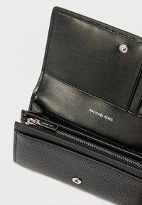 Μαύρο δερμάτινο πορτοφόλι με υφή, διαμέρισμα με φερμουάρ και θήκες για κάρτες. Διαθέτει κούμπωμα με πατιλέτα και ανάγλυφο λογότυπο.