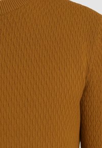 Maglione lavorato a maglia in un caldo colore senape, caratterizzato da un motivo a rombi testurizzato, colli a coste e tessuto morbido.