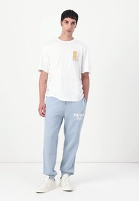 Hvid T-shirt med logo på brystet og lyseblå sweatpants med hvid tekstlogo, parret med hvide sneakers. Enkel og afslappet design.