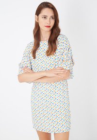 Vestido de manga corta con una base blanca y un vibrante patrón disperso de formas naranjas y azules. Tejido suave con un corte holgado.