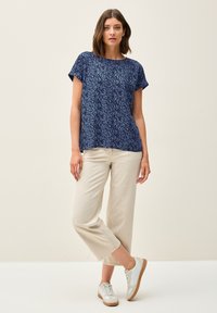 Haut marine à manches courtes avec un motif de feuilles ; associé à un pantalon large beige clair et des baskets blanches avec des accents beiges.