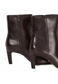 Une paire de bottines en cuir marron foncé avec des zips sur les côtés et des talons carrés de hauteur moyenne.