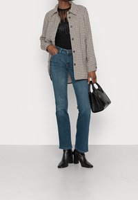 Chaqueta de gran tamaño de pata de gallo, top negro con flecos, vaqueros azul claro, botas de tacón negras y un bolso pequeño negro con un acabado texturizado.