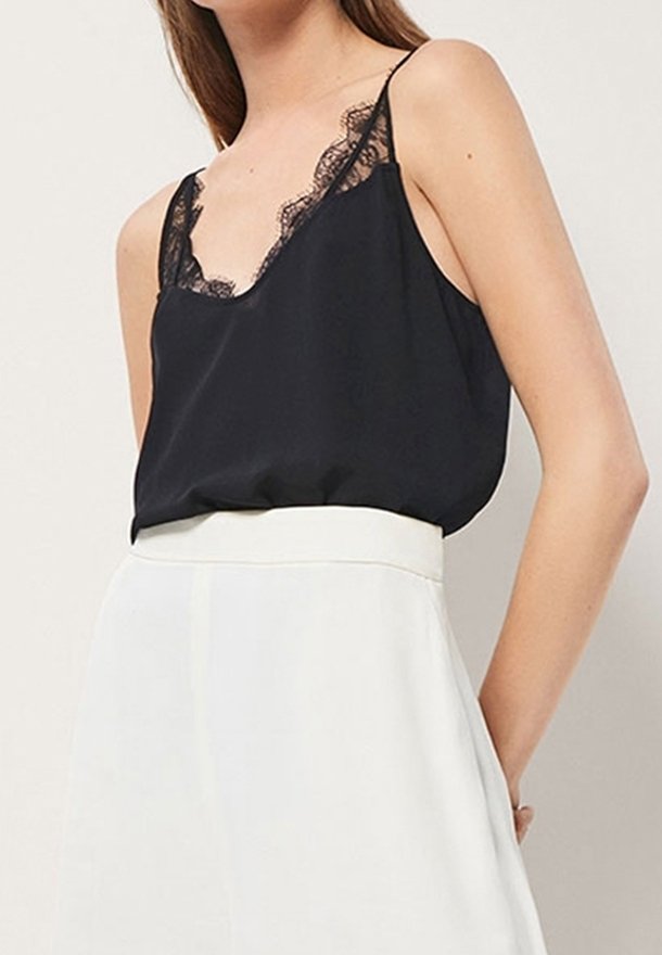 Mustat satiinikankaiset topit, joissa on pitsireunus kaula-aukossa ja ohuet olkaimet, yhdistettynä valkoisiin korkeavyötäröisiin hameisiin.