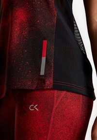 Sort tank top med et rødt sprøjtedesign, med røde og grå accenter i kanten. Røde leggings med en lignende tekstur og CK-logo.