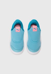 Une paire de baskets slip-on pour tout-petits avec des tiges bleu clair, des tirants roses avec le logo Puma, une doublure intérieure turquoise et des semelles blanches sur fond blanc.
