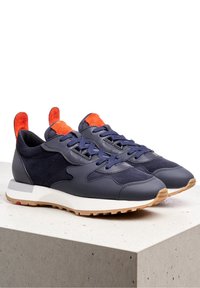 Navy blue sneakers with leather and suede panels, dark blue laces, orange pull tabs and tongues, white midsoles, and gum rubber outsoles.